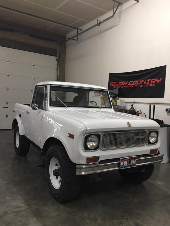 A white International Scout truck parked inside a garage with a Rough Country banner on the wall.
