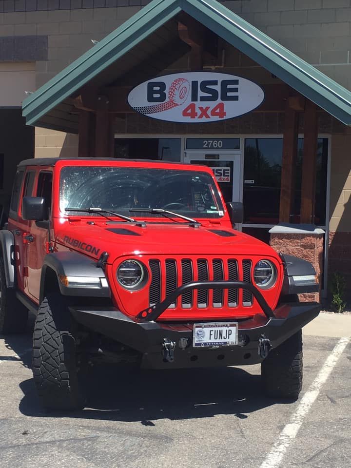 A bright red Jeep Rubicon with large tires and a black bumper parked in front of a Boise 4x4 shop.