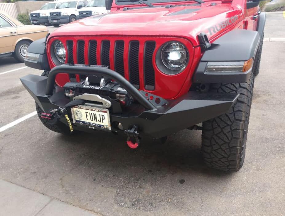 A red Jeep Wrangler with a custom black steel bumper and winch parked in an outdoor lot.