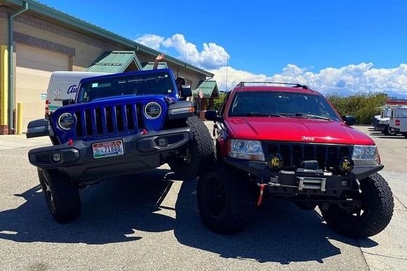 A blue Jeep Wrangler climbs over the front tire of a red Jeep Grand — 4 x 4 shops near me