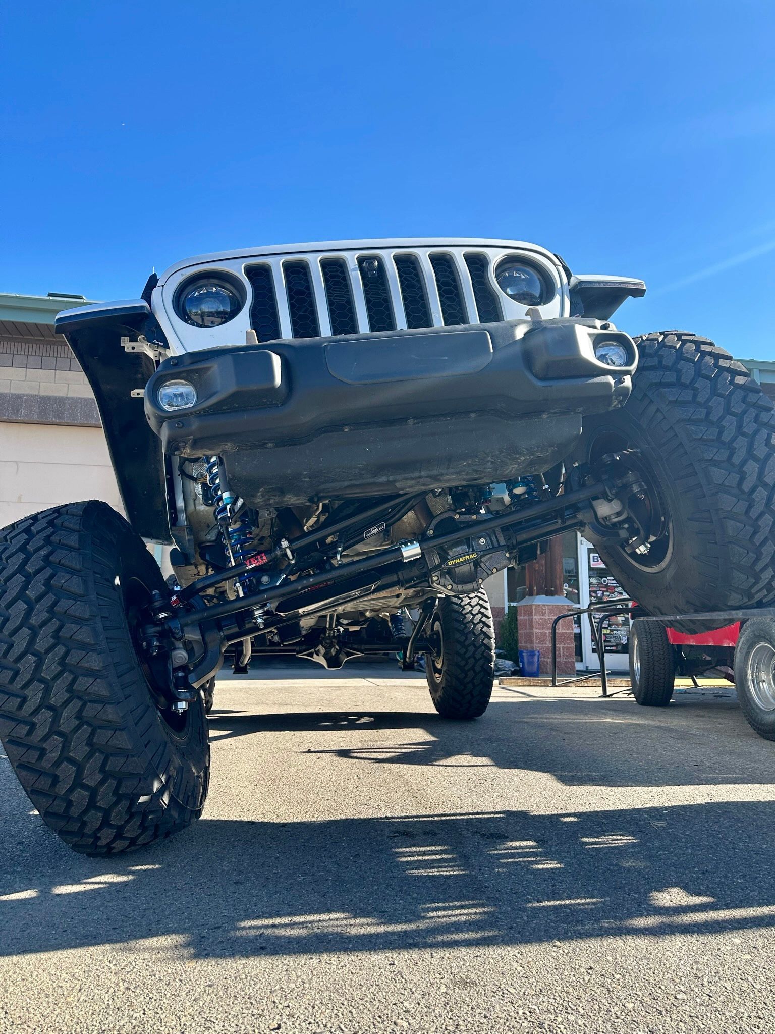 A modified Jeep with large off-road tires parked at an angle on a ramp against a clear blue sky.