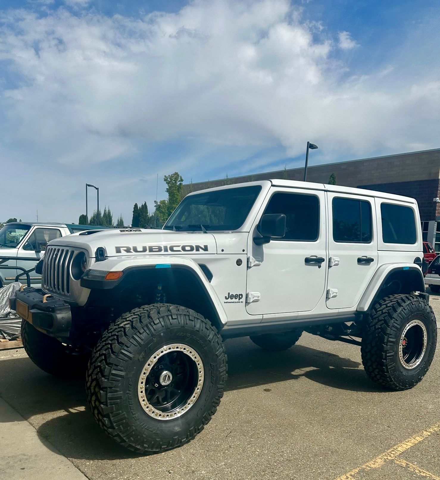 A white Jeep Wrangler Rubicon with large off-road tires and aftermarket wheels parked in an outdoor lot.