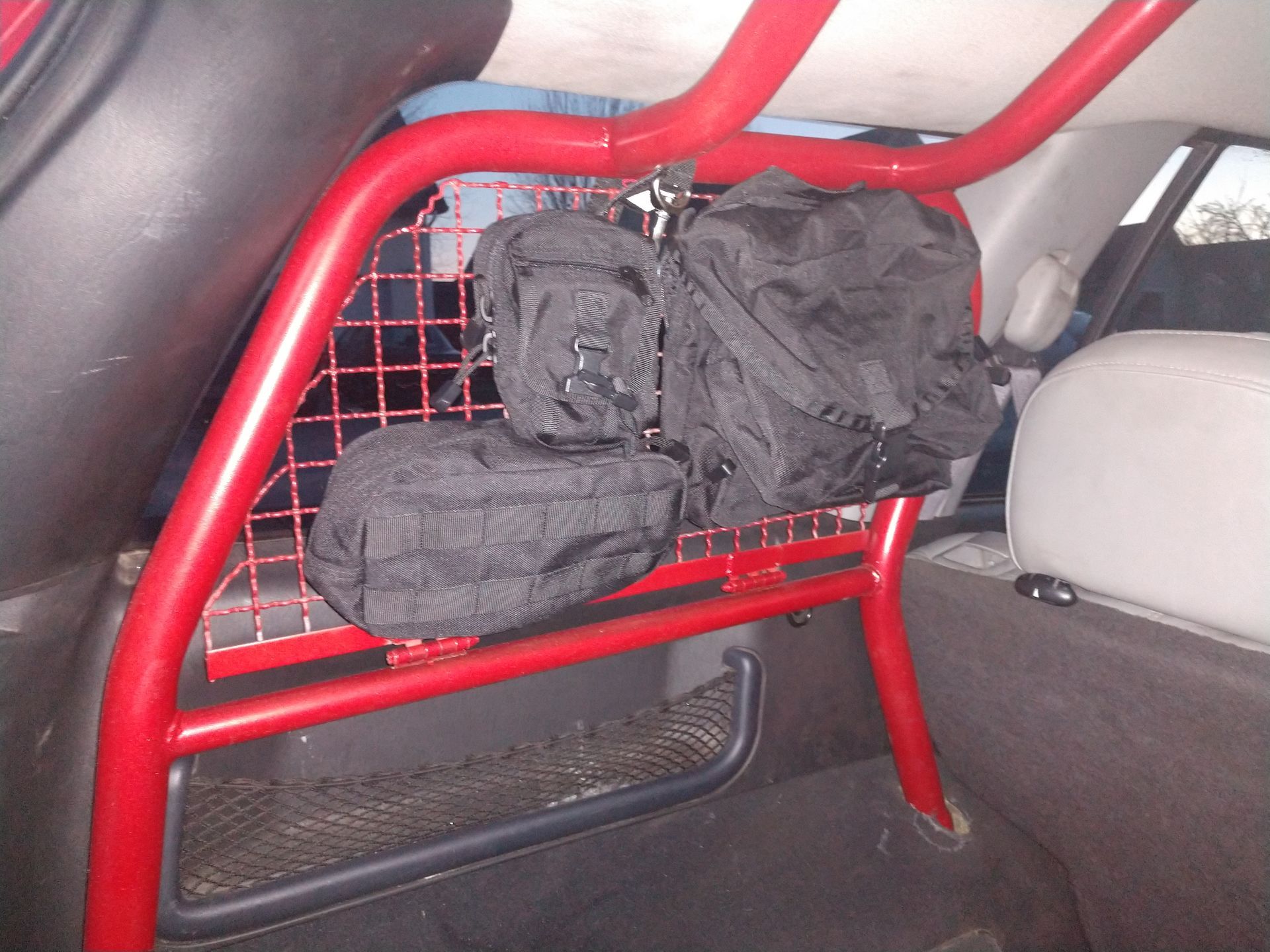 Black gear bags attached to a red metal roll cage partition inside a vehicle’s cargo area.