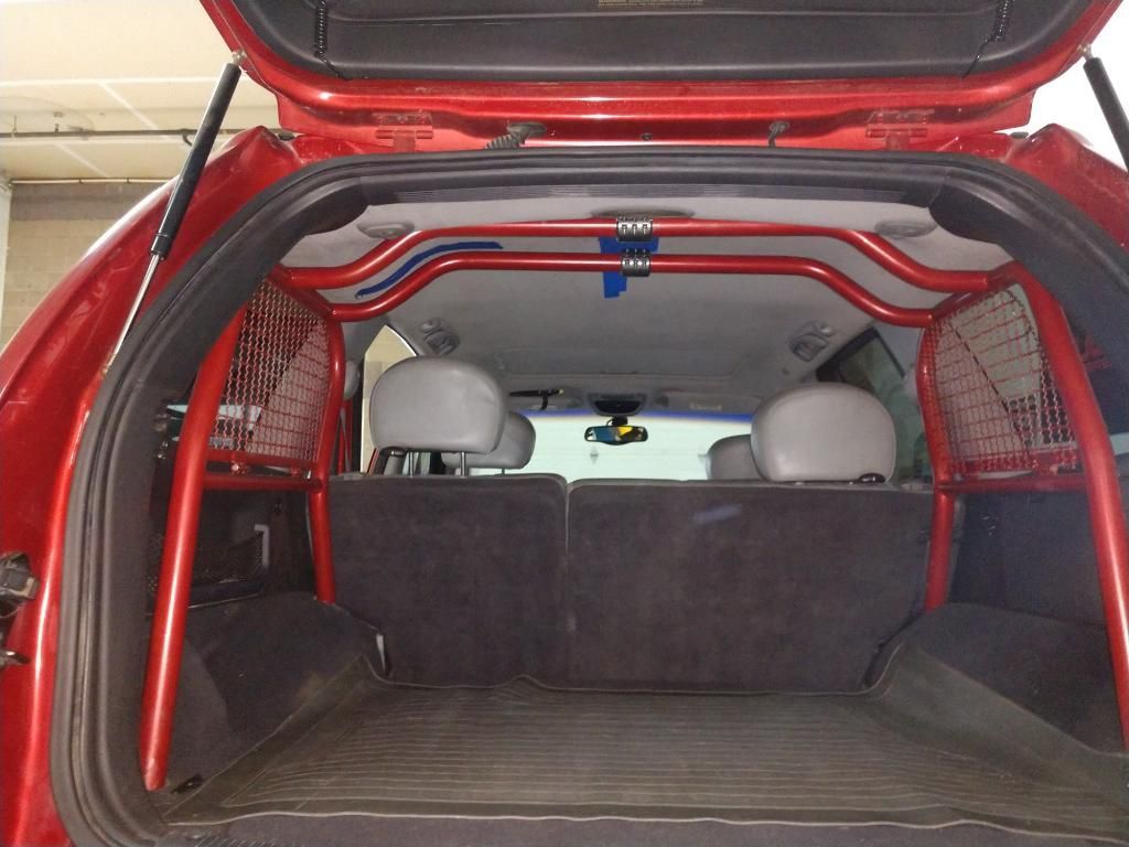 A red, tubular metal cage installed inside the cargo area of an SUV, featuring side mesh panels.