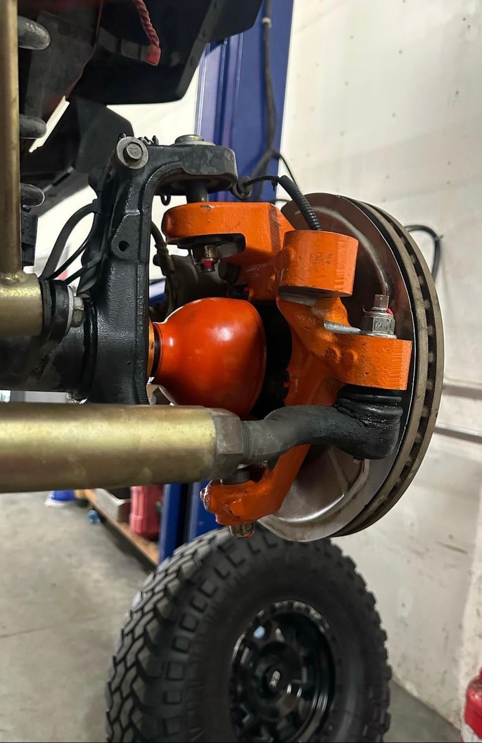 Close-up of a vehicle's front suspension assembly, featuring orange painted components, in an automotive workshop.