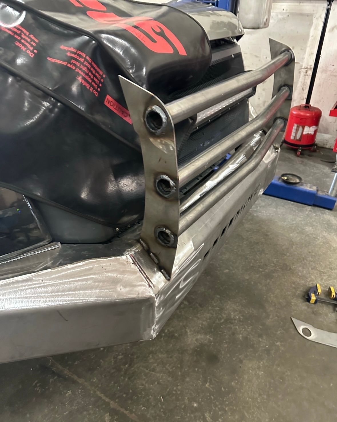 A close-up view of a metal bull bar being fabricated and welded onto a vehicle's front bumper in a workshop.