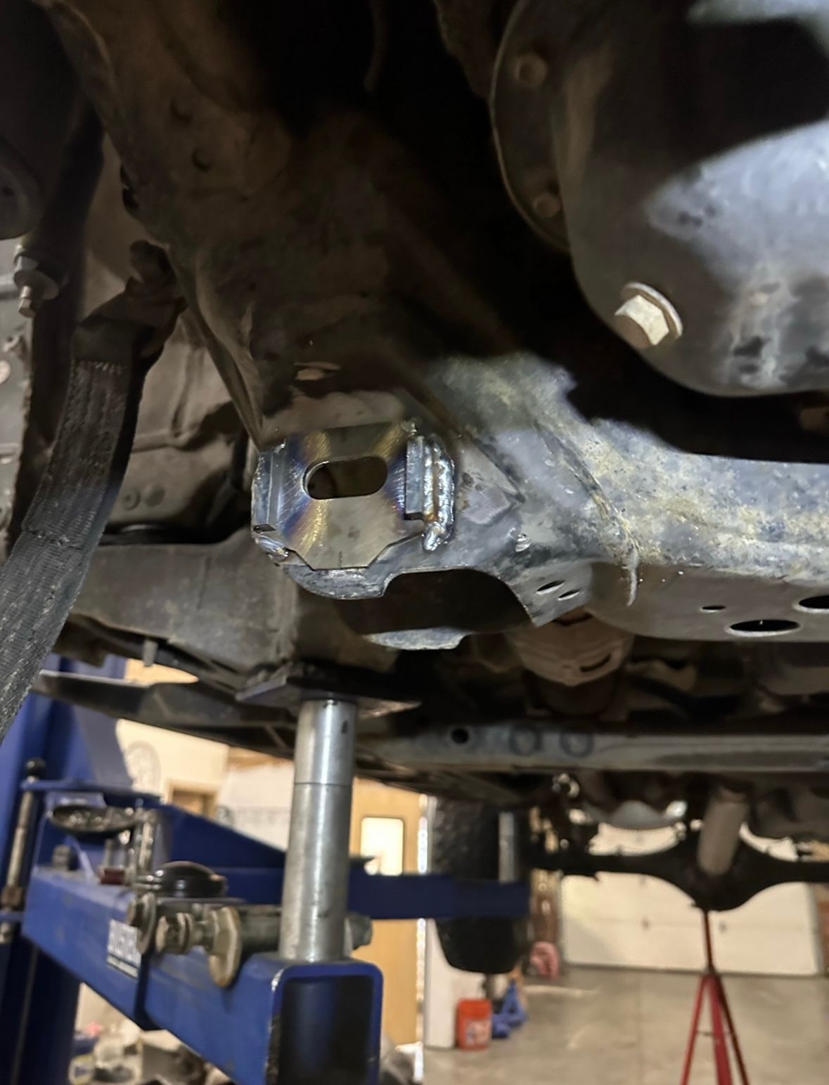 A metal plate welded onto the undercarriage of a vehicle, which is raised on an automotive lift in a workshop.