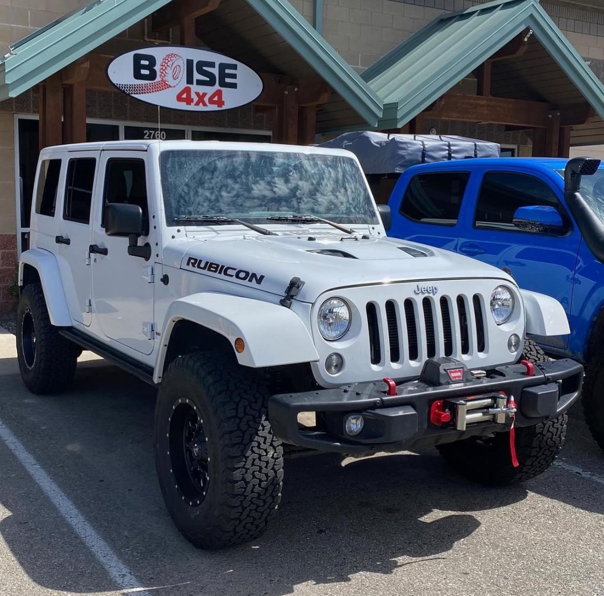 A modified white Jeep Wrangler Rubicon parked in front of a building with a 