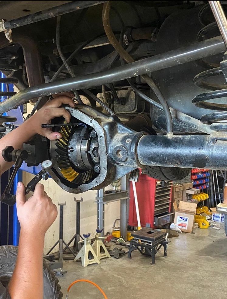 A mechanic uses a dial indicator to measure backlash on the ring gear of an automotive differential in a garage.