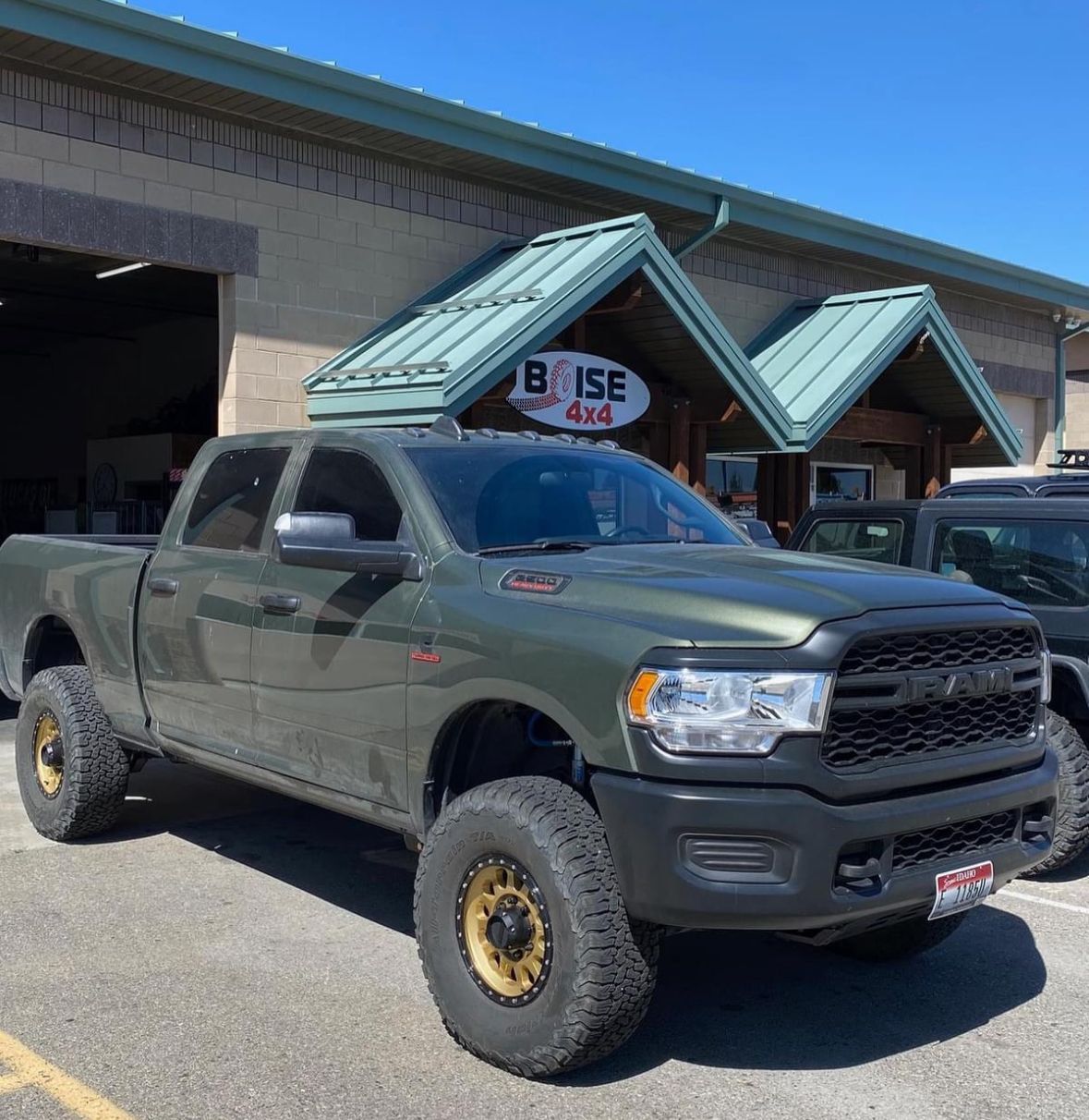 An olive green lifted Ram truck parked in front of a Boise 4x4 shop with gold wheels and black trim.