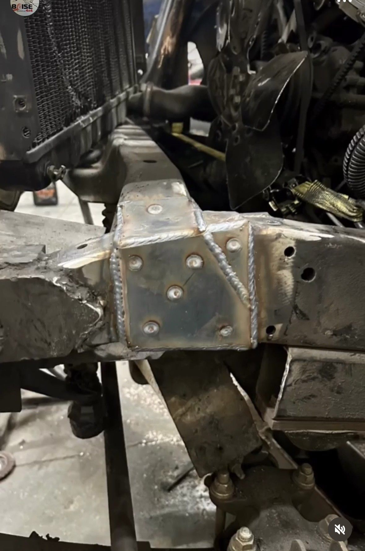 A metal frame component with a freshly welded reinforcement plate on a vehicle chassis in a garage setting.