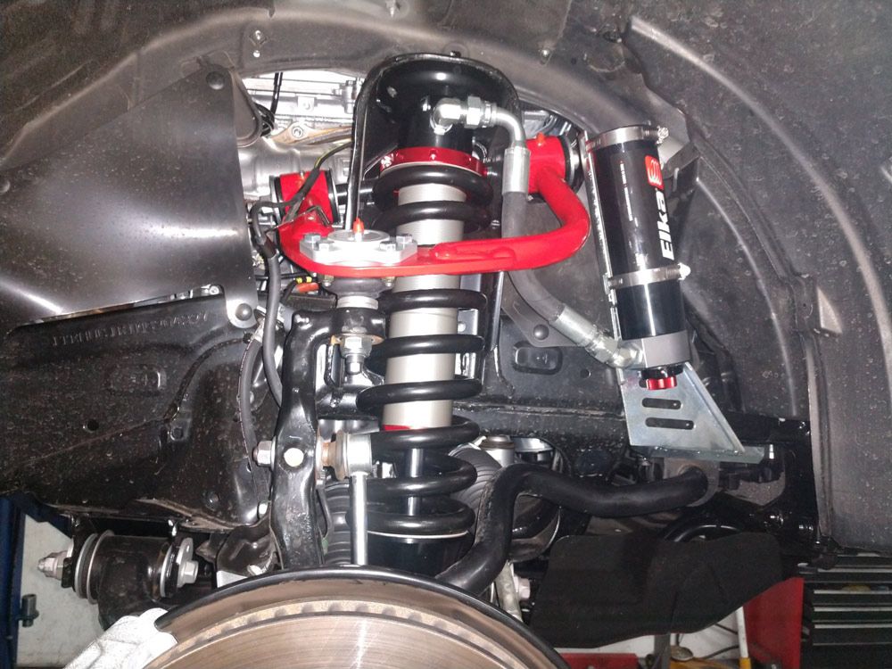 A vehicle's front suspension system featuring a red control arm and an Elka shock absorber with a remote reservoir.