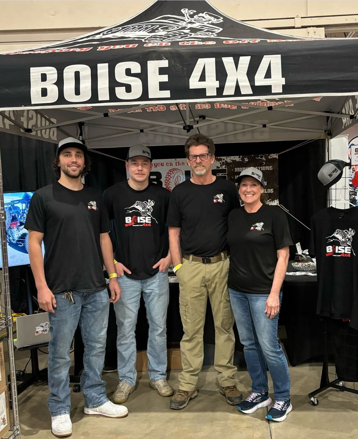 Four people in matching black t-shirts stand side-by-side under a 