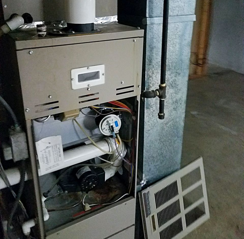 Furnace with open panel, pipes and wires visible. Beige, in a basement.