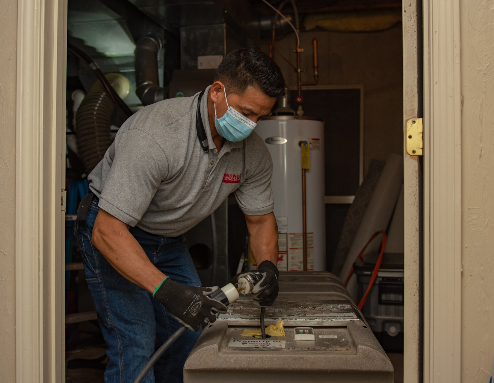 Man in mask cleaning an HVAC unit in a basement. He is wearing gloves and jeans.