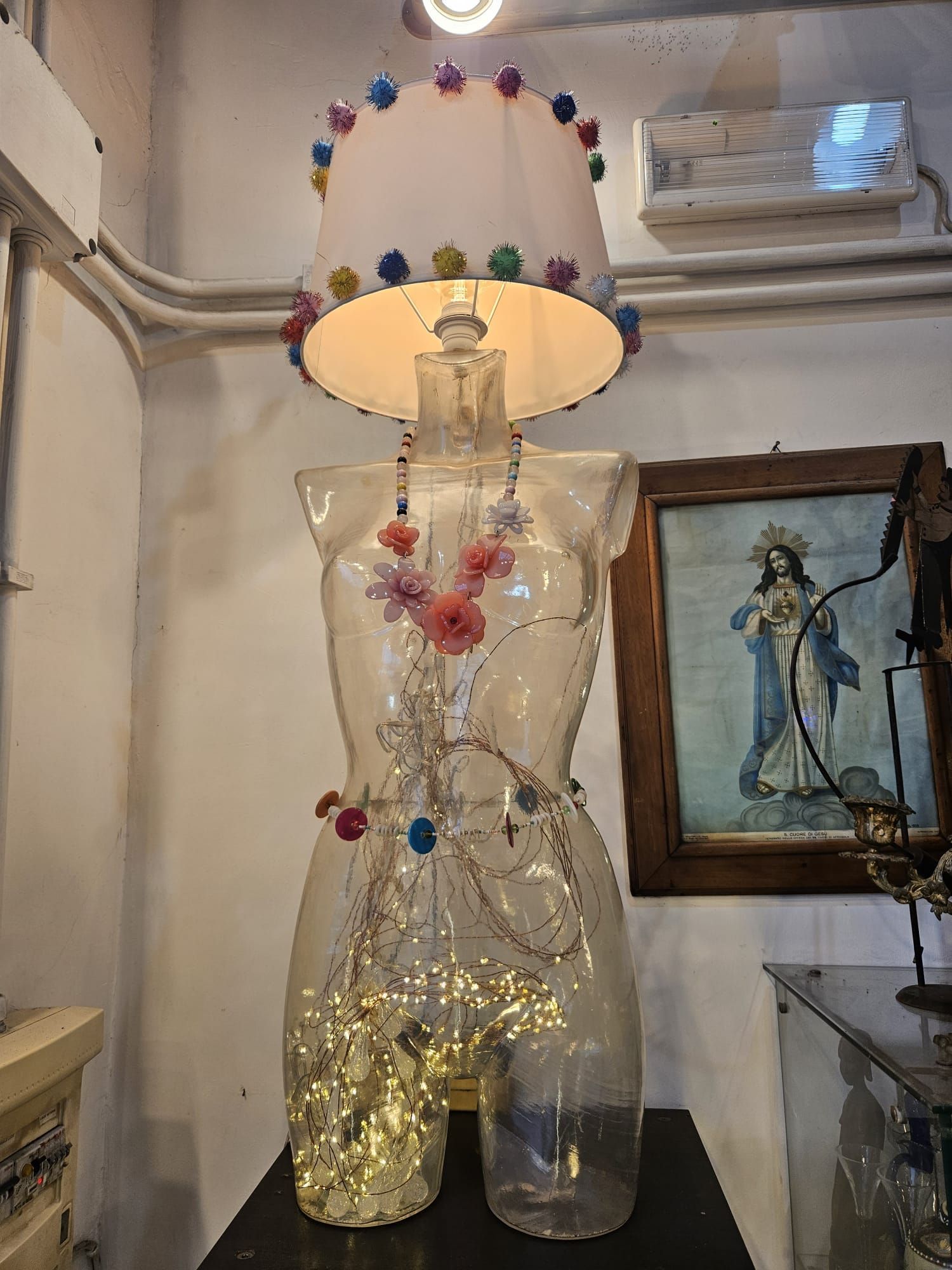 Lampada realizzata a forma di torso trasparente, con paralume. Impreziosita da luci e fiori.