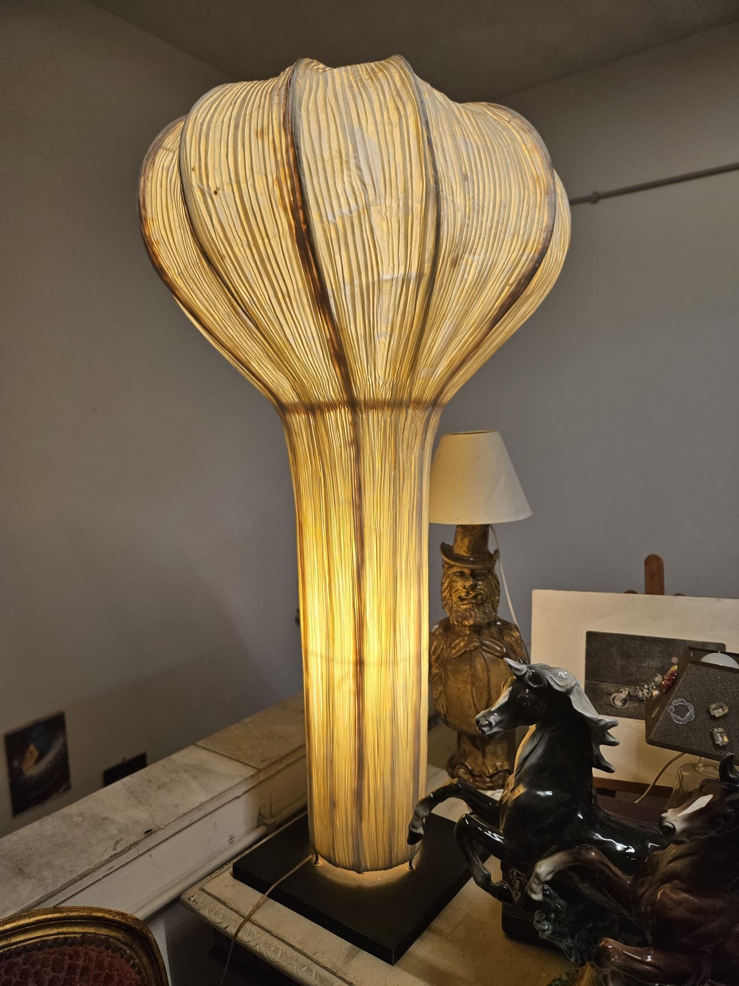 Lampada da terra alta color beige con paralume decorato, illuminata.