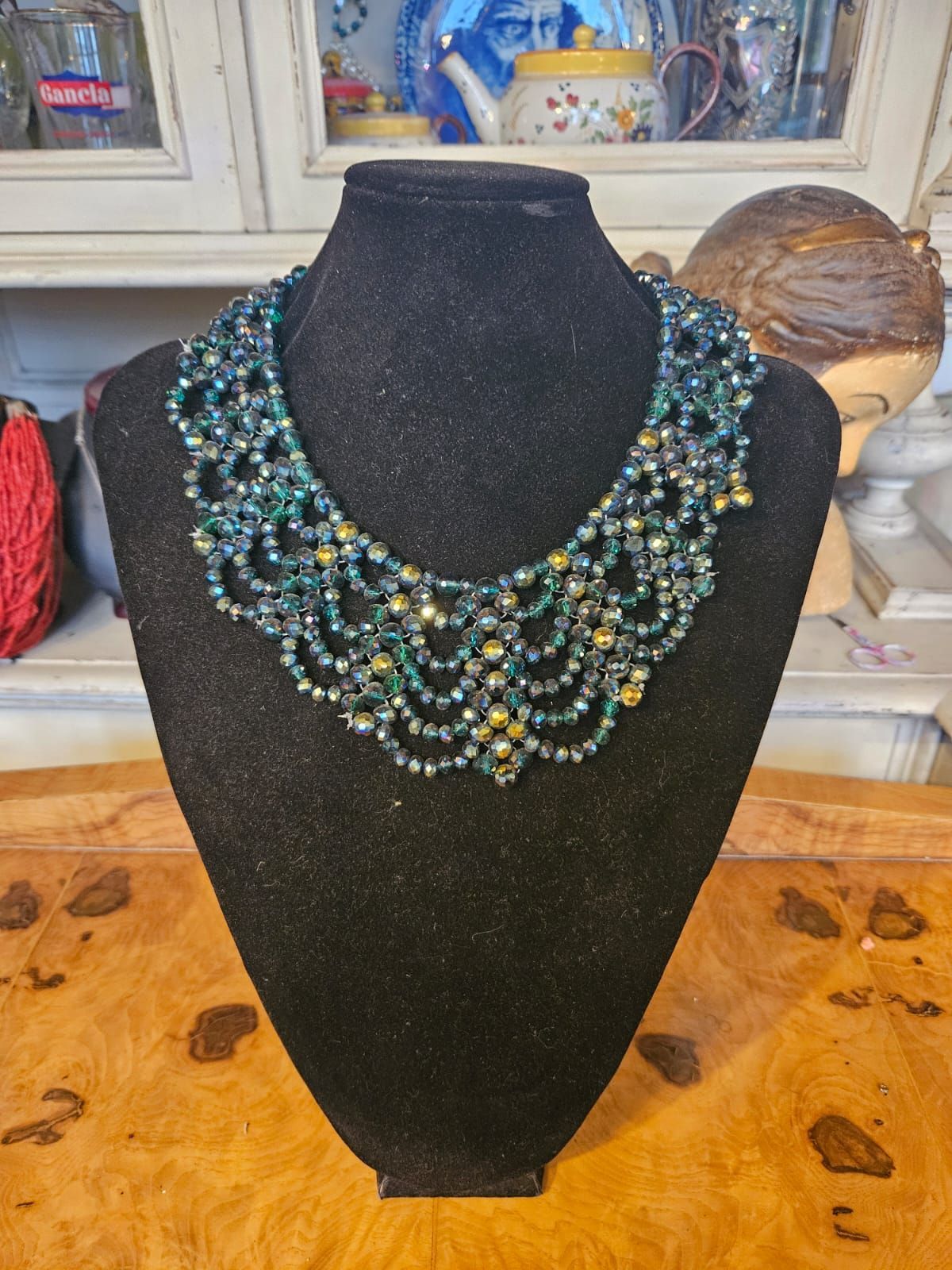 Collana di perline su un manichino nero, nei colori verde acqua e oro. Esposta su una superficie di legno.