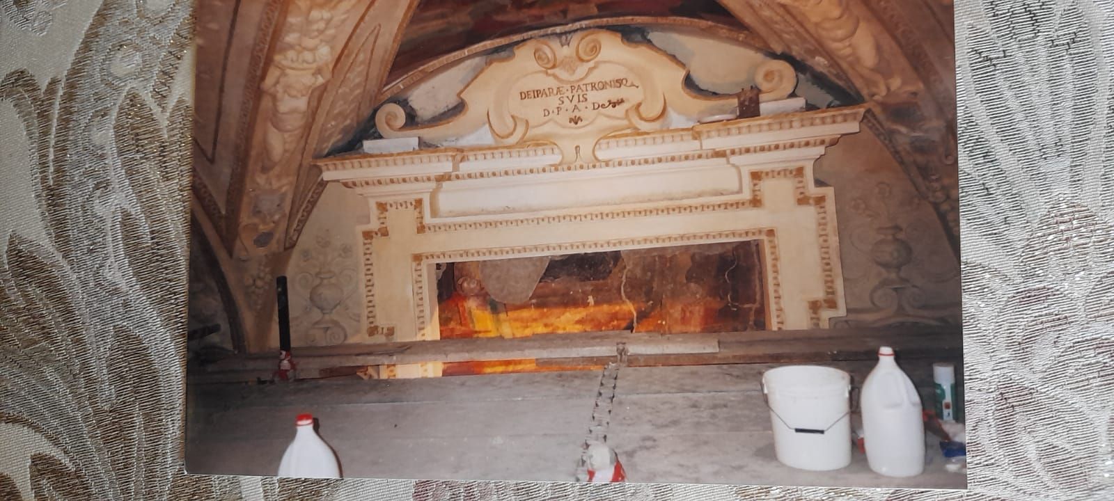 Camino con fuoco acceso, in una stanza con una mensola decorativa. Bottiglie e secchio sono posizionati di fronte.