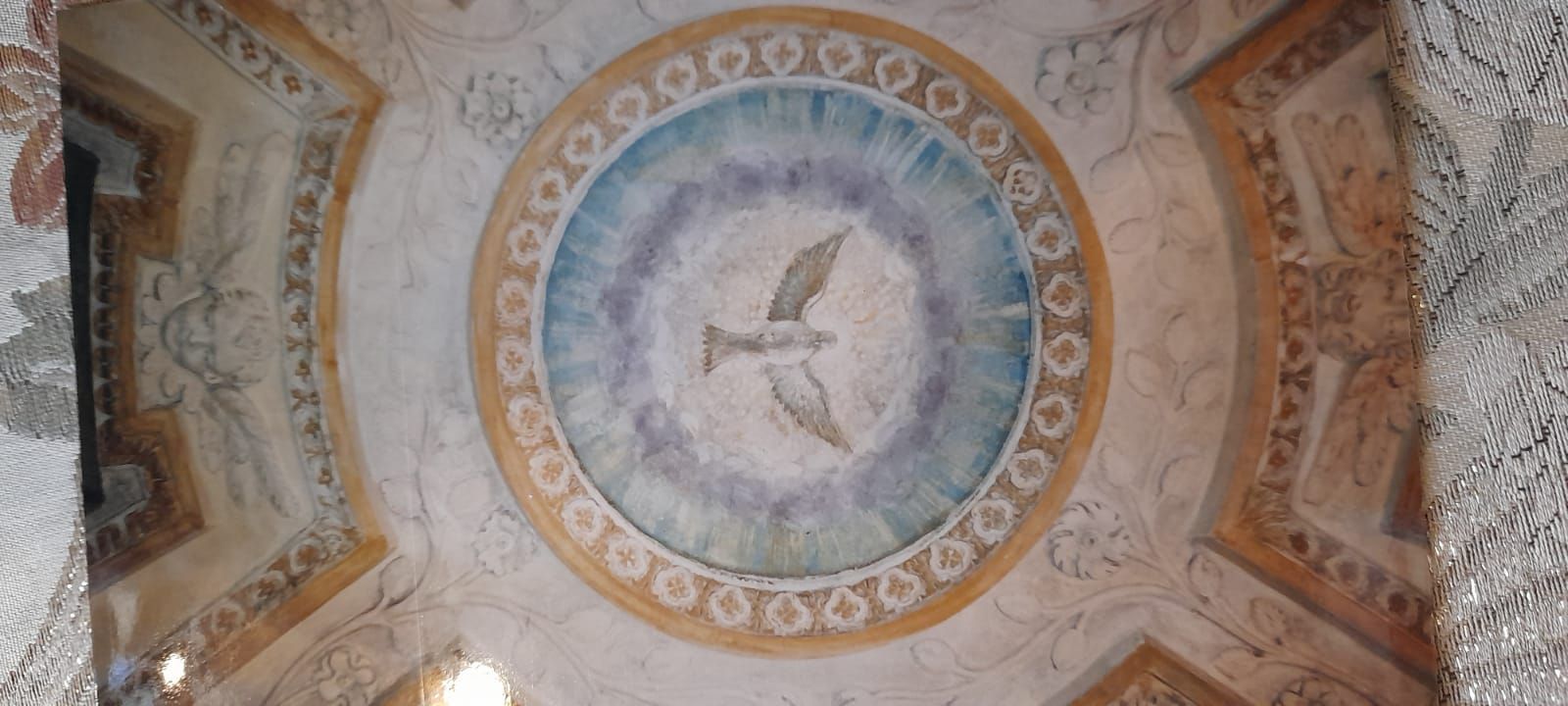 Affresco sul soffitto con il simbolo della colomba, circondato da dettagli dipinti e ornati.
