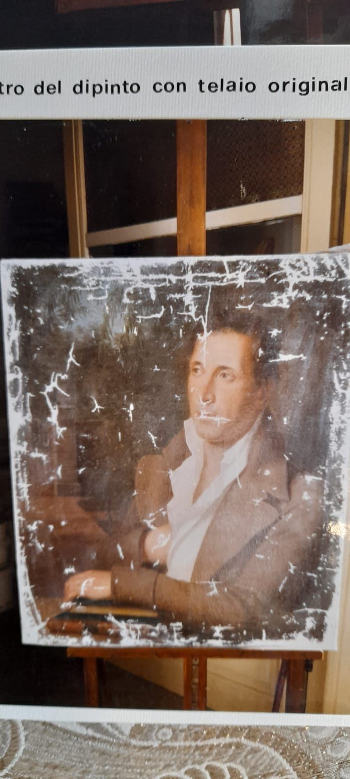 Un ritratto sbiadito su un cavalletto; un uomo con una giacca marrone e una camicia bianca.