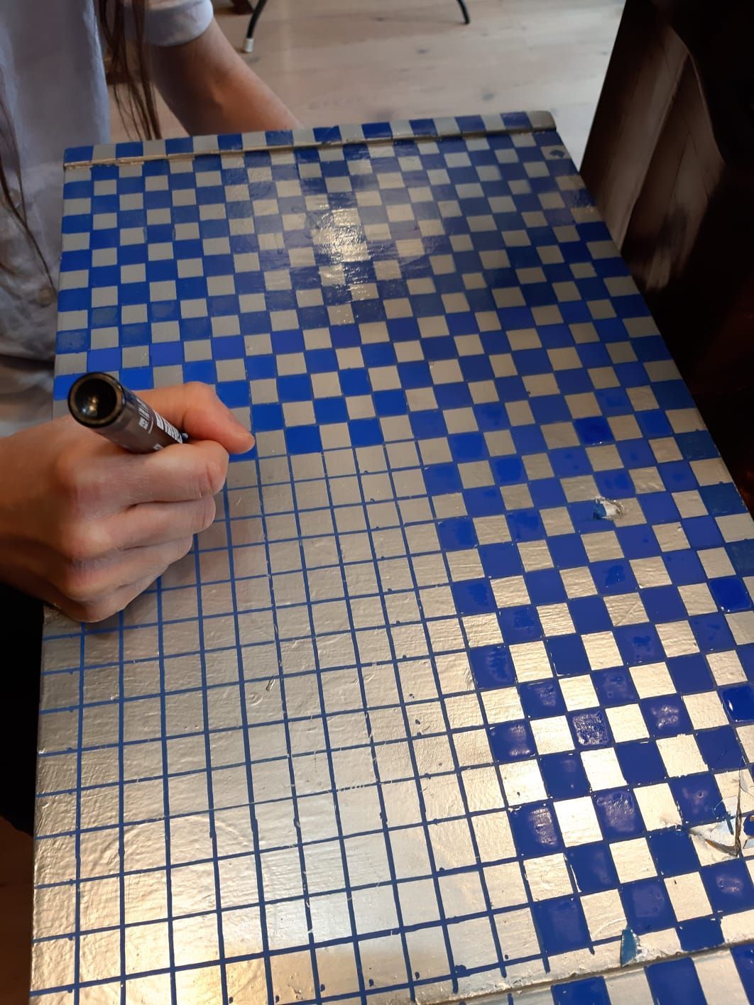 Mano di una persona che tiene una penna e scrive su una superficie a scacchi blu e argento.