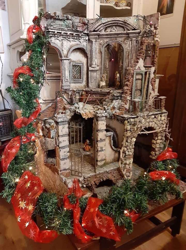 Presepe natalizio con edifici segnati dal tempo, decorato con nastri rossi e verde.