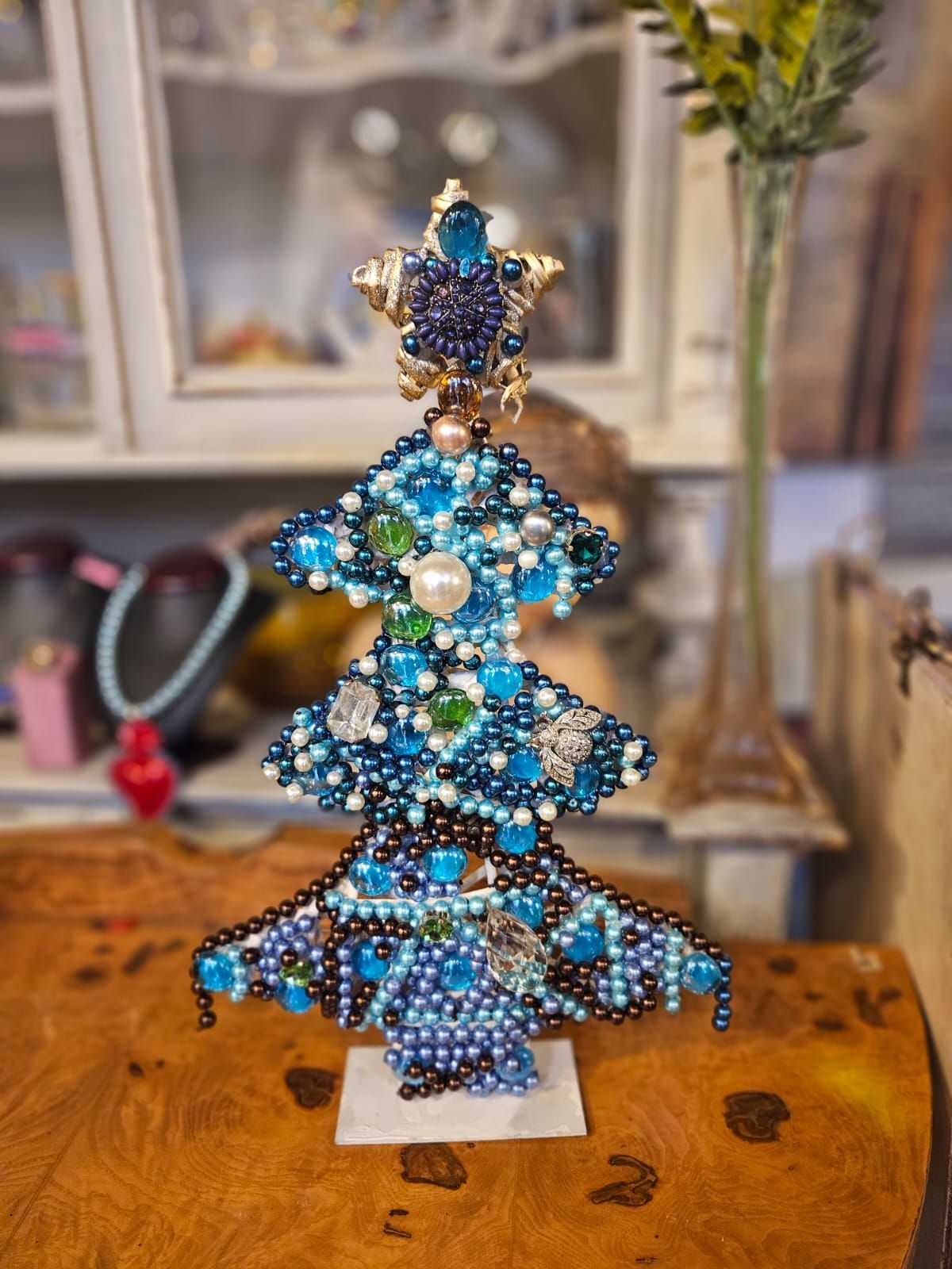 Decorazione per albero di Natale blu con perline e puntale a forma di stella, su un tavolo di legno.