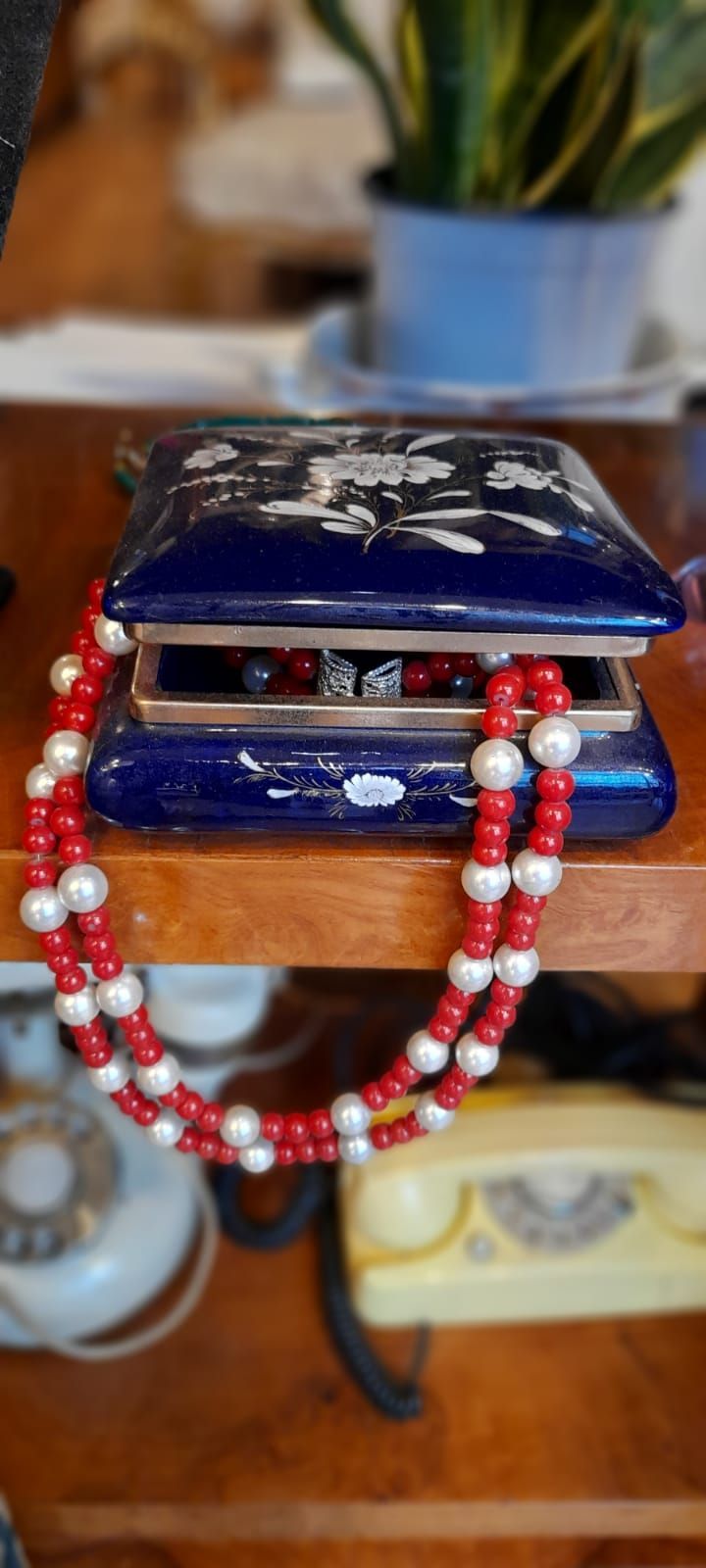 Portagioielli blu con collana di perline rosse e bianche, telefoni fissi gialli e bianchi e pianta in vaso.