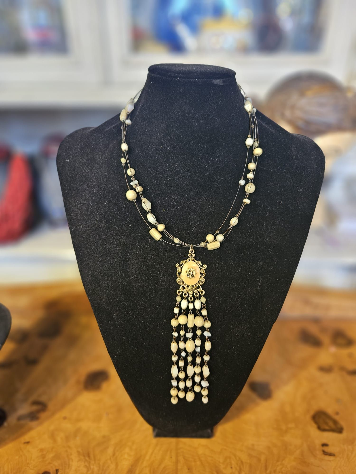 Collana di perline con pendente e frange esposta su un manichino nero.