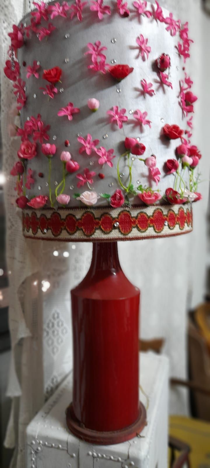 Lampada da tavolo rossa con decorazioni floreali e paralume argentato.