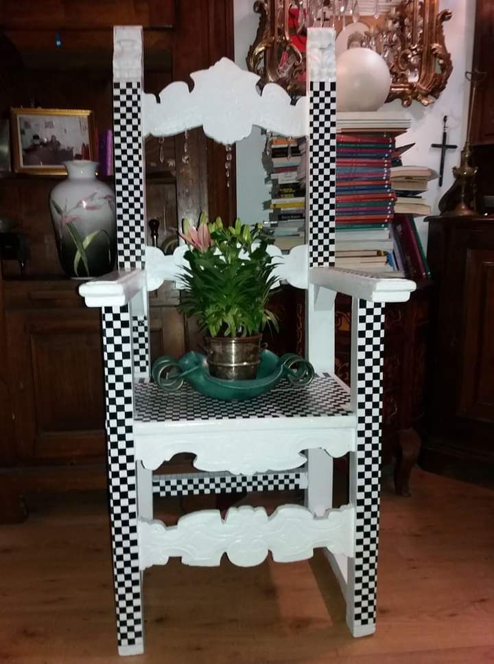 Sedia dipinta di bianco e a scacchiera con piante e decorazioni ornamentali sullo sfondo.
