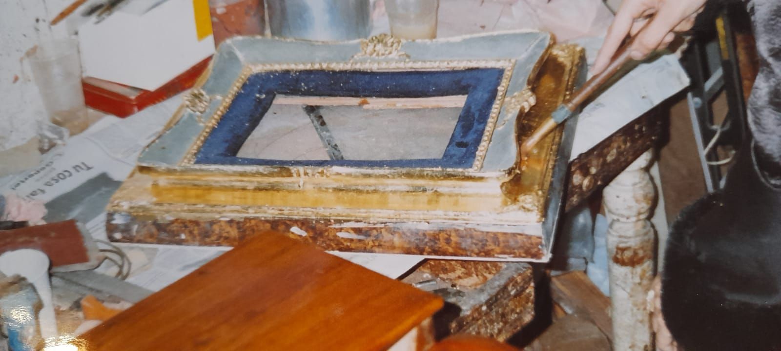 Una cornice rettangolare decorata con l'interno blu è immersa nel disordine. La cornice presenta dettagli dorati e danni visibili.