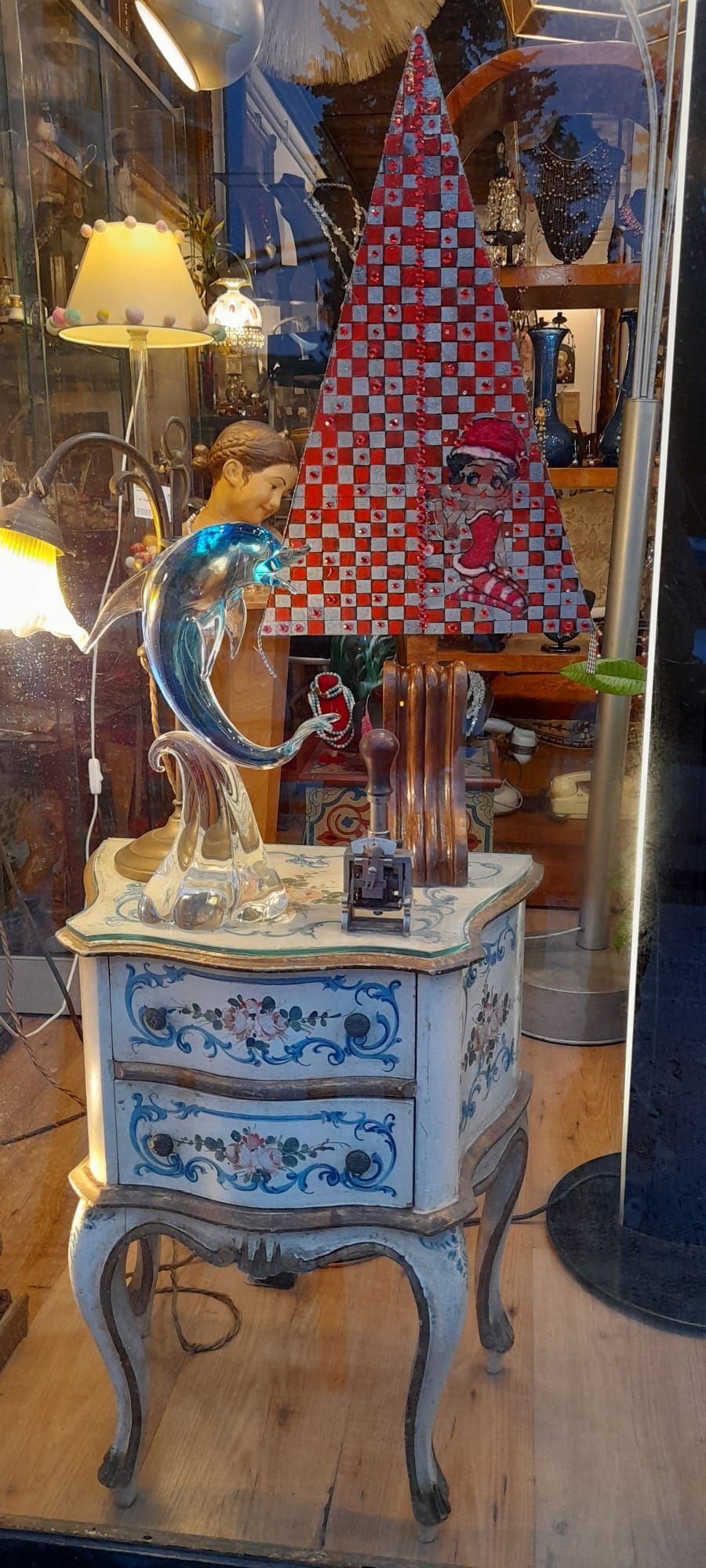 Una vetrina con un comodino dipinto, una scultura di pesce e un paralume a scacchi.