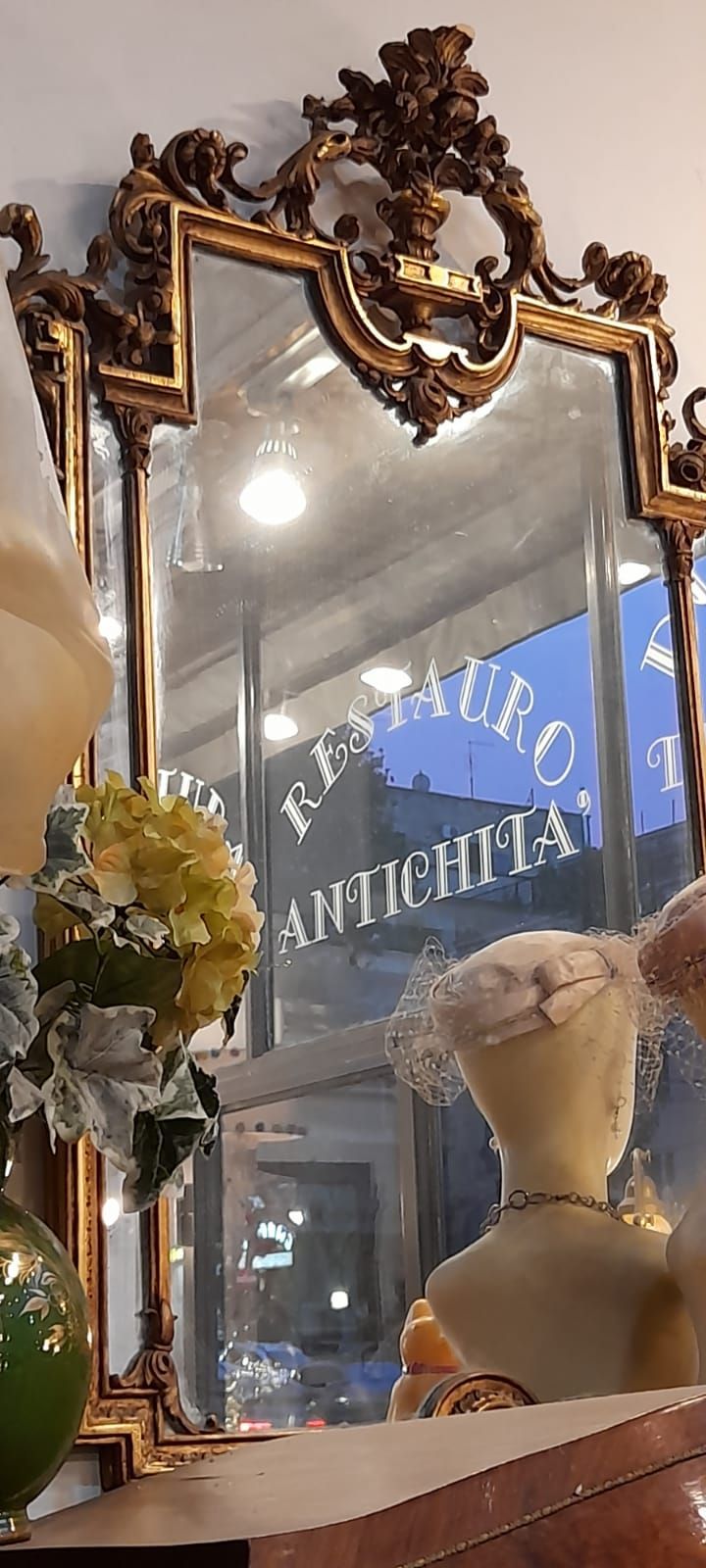 Specchio decorato con cornice dorata che riflette una vetrina con la scritta 