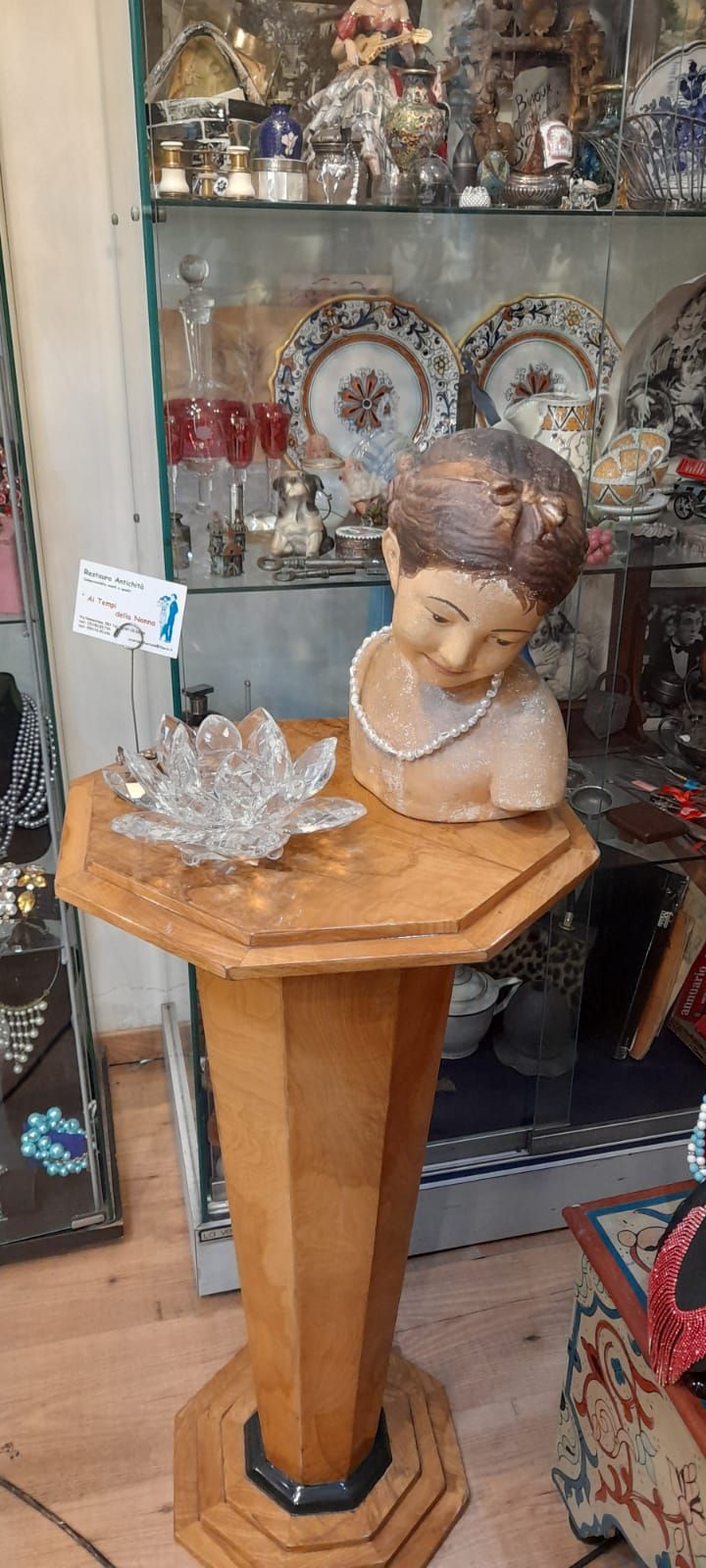 Un piedistallo di legno con un busto e una ciotola di cristallo esposti in un negozio.