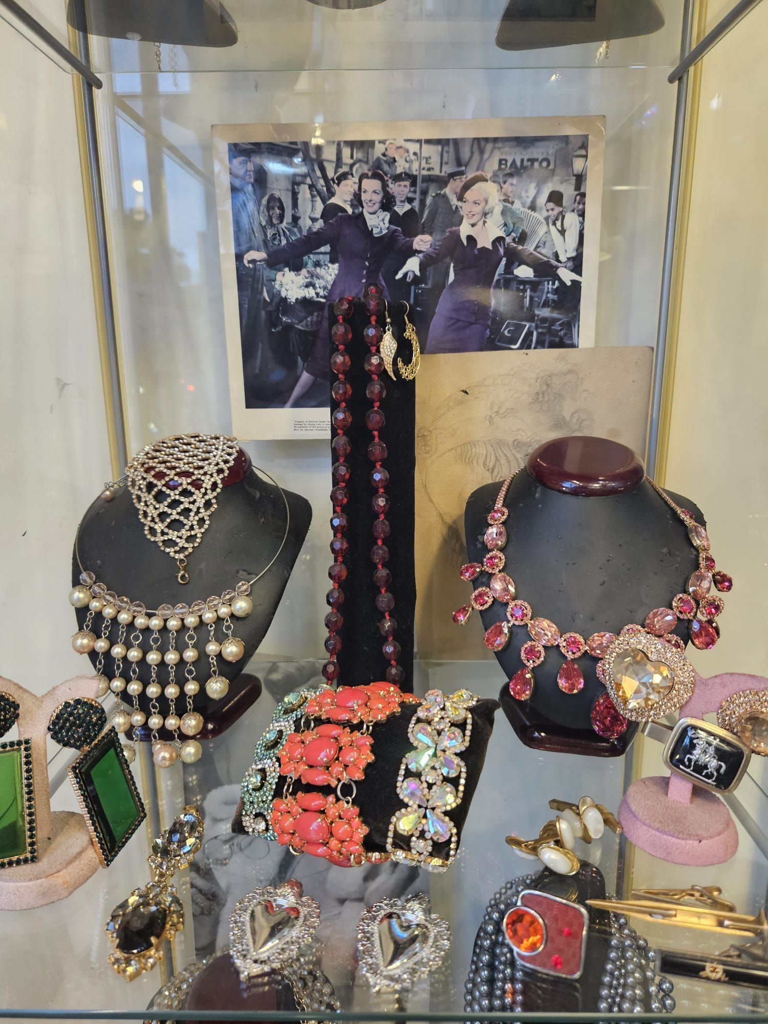 Vetrina portagioielli con collane, braccialetti, orecchini e sfondo fotografico vintage.