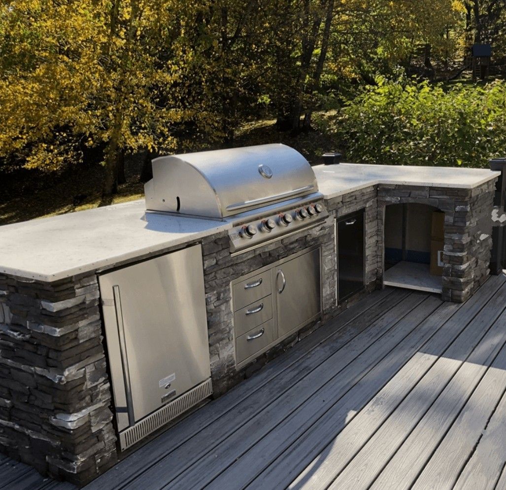 Outdoor stone-built grill station with stainless steel cabinets and a built-in pizza oven on a wooden deck