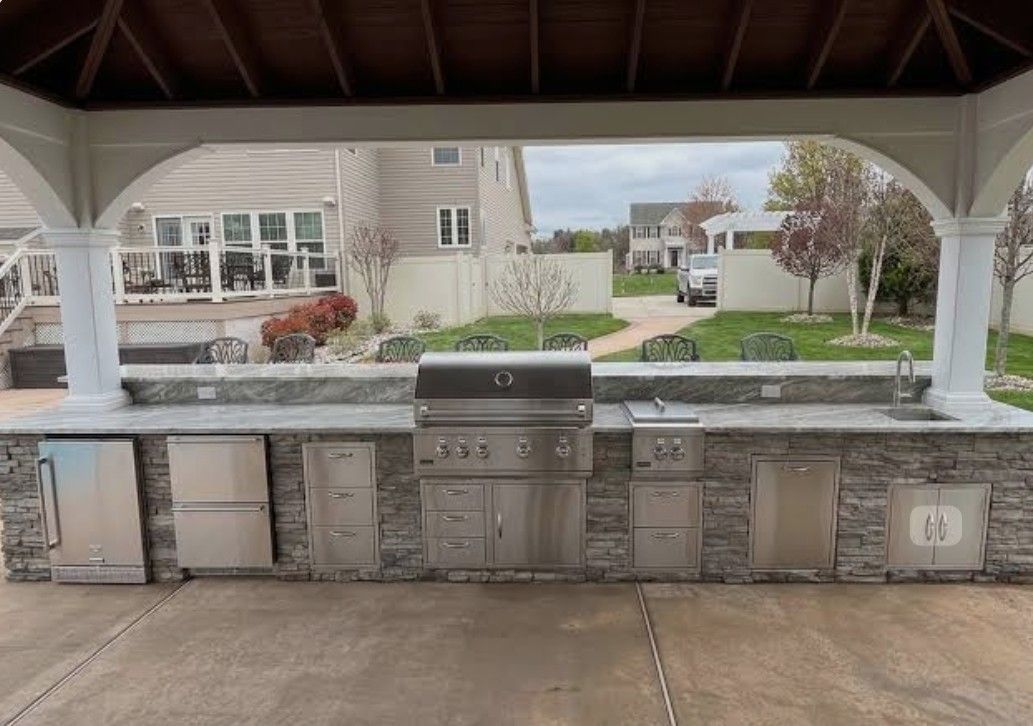 Covered outdoor stone grill station with multiple built-in grills and a park view behind it