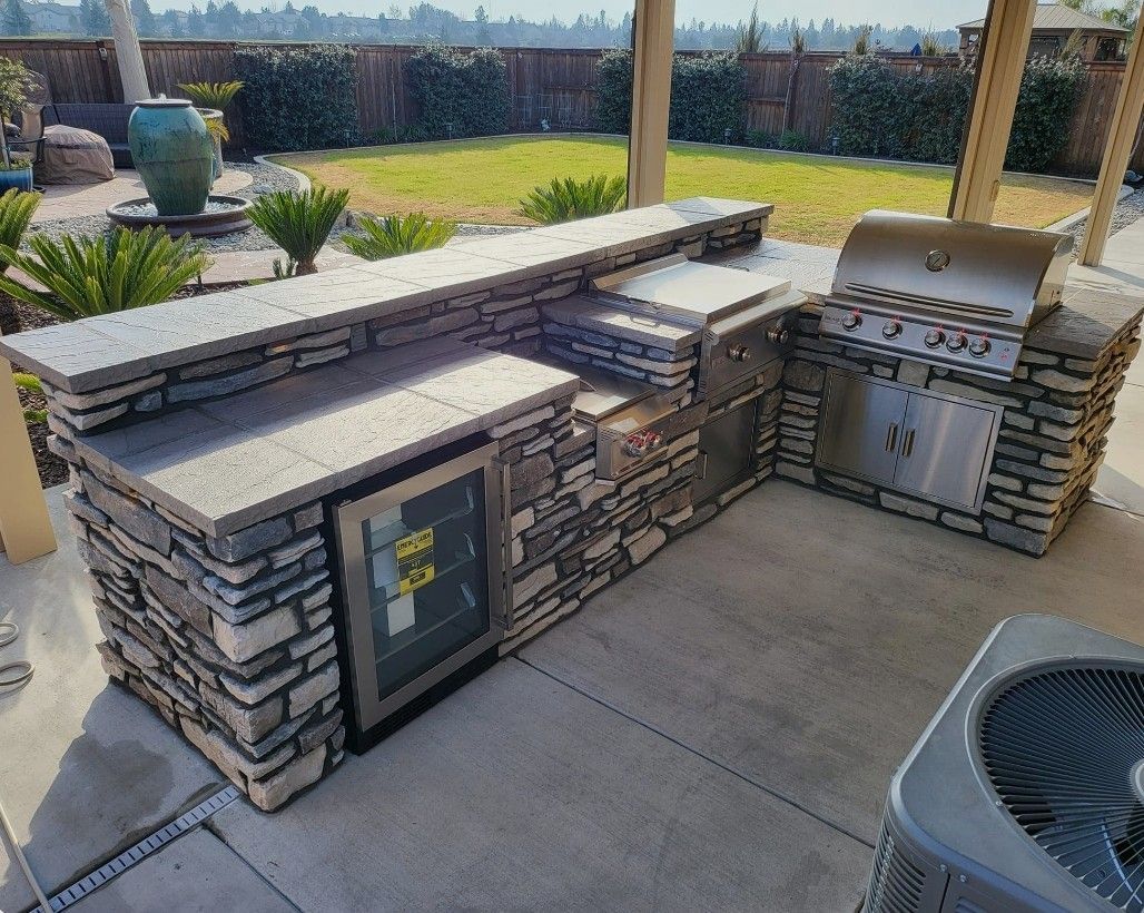 Outdoor stone patio with built-in grill, counter, and cabinets under a covered pergola