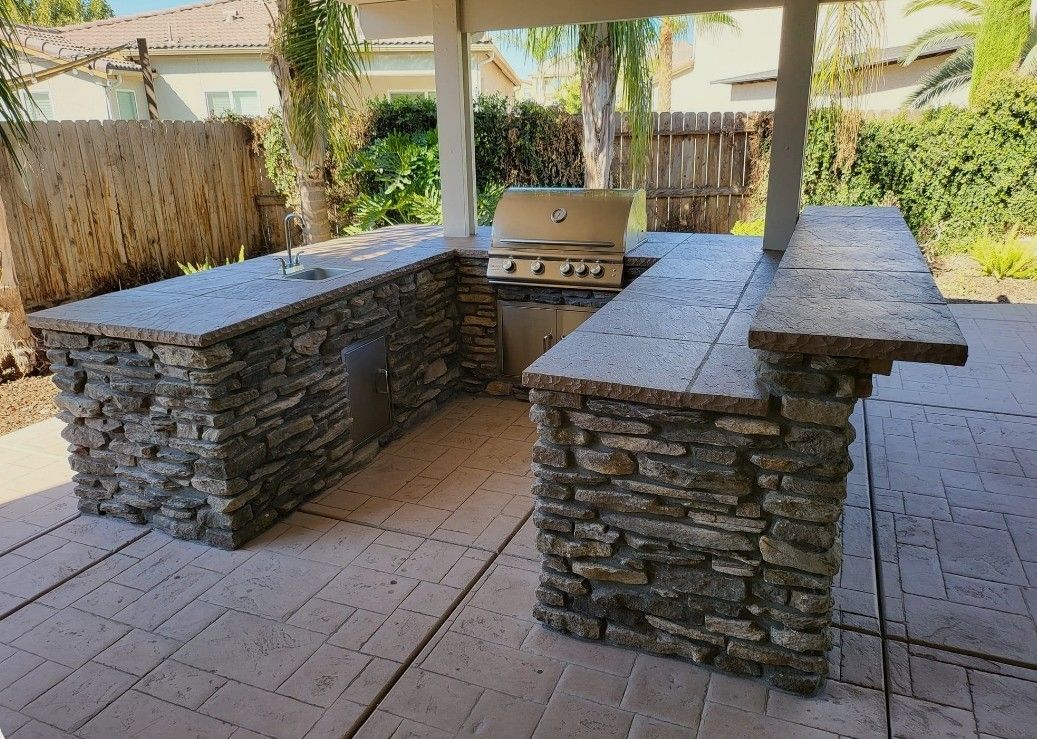Stone outdoor kitchen with built-in grill under a covered patio