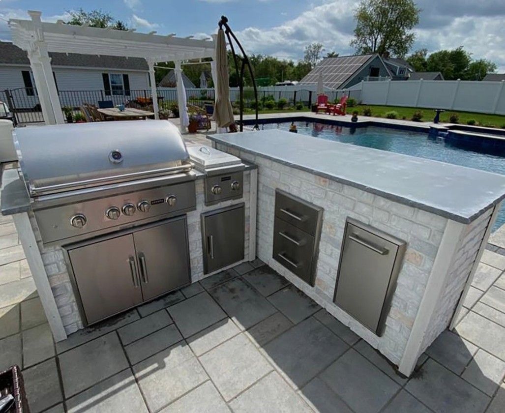 Outdoor patio with stainless steel grill, sink, and cabinet beside a swimming pool.