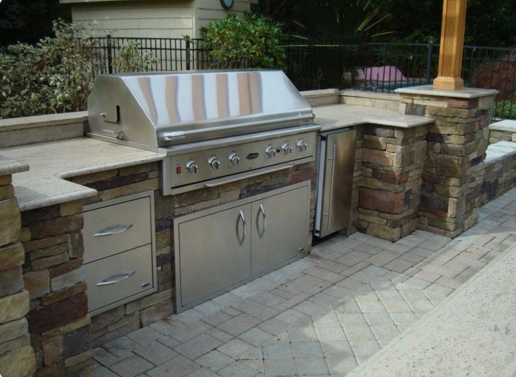 Outdoor stainless steel grill and prep counter built into a stone patio kitchen