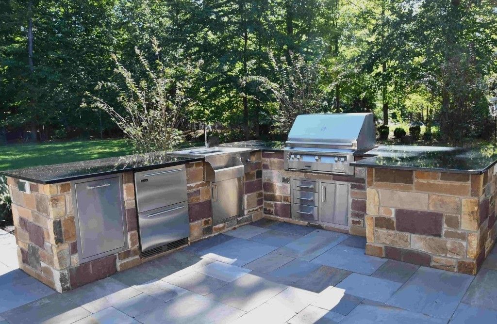 Outdoor stone kitchen with built-in grill, sink, and counter under trees