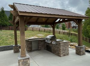 Wooden pergola over a concrete patio in a landscaped backyard, with lawn, wall, and house in the background