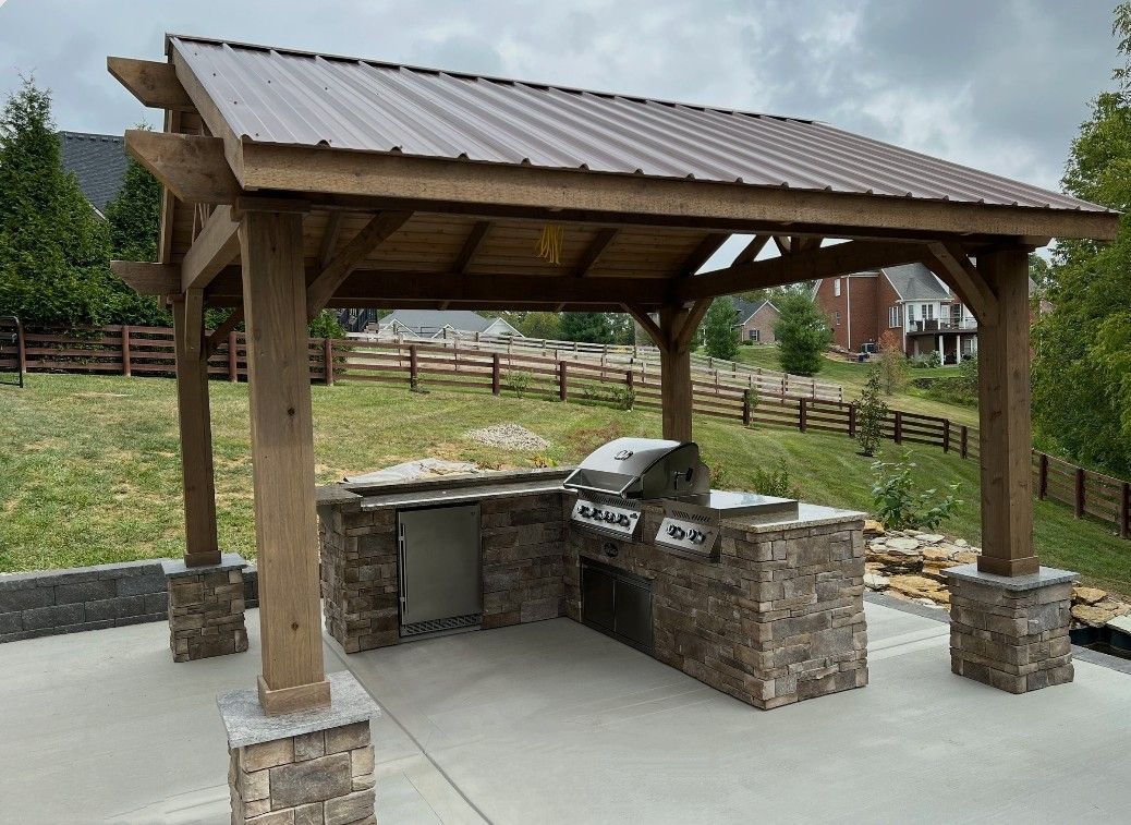 Covered stone barbecue shelter on a concrete patio in a grassy yard