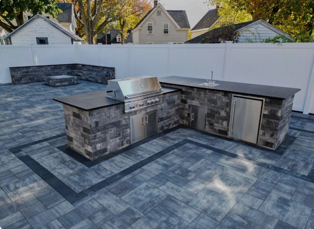 Rooftop with a stone utility enclosure and vents on a flat gray membrane roof, with houses and trees in the background