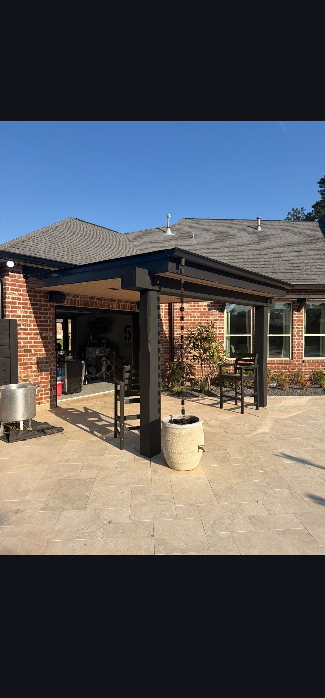 Brick house entrance with covered patio, tiled roof, and dry yard in bright sunlight