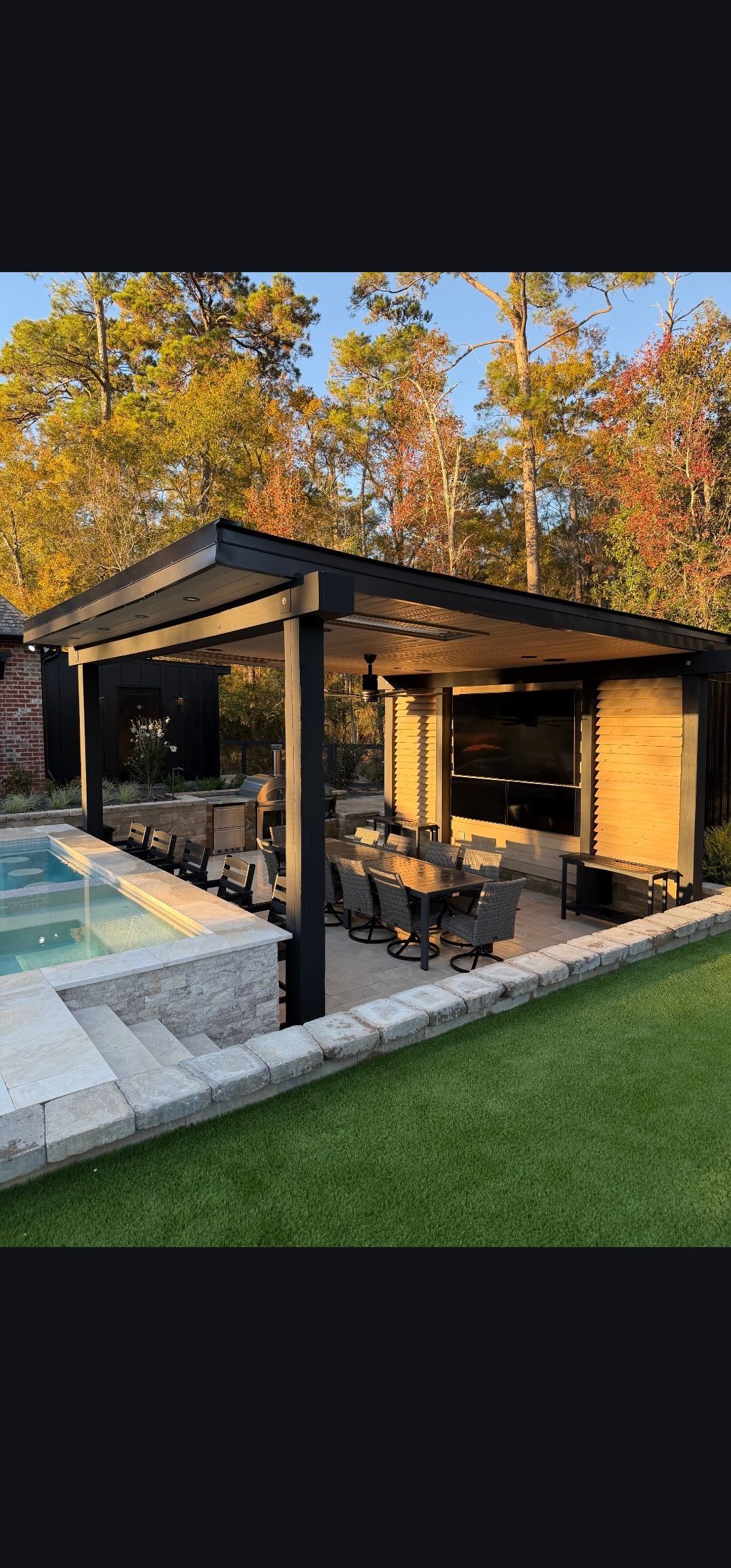 Covered patio with black beams, outdoor seating, and a pool beside a grassy yard at sunset