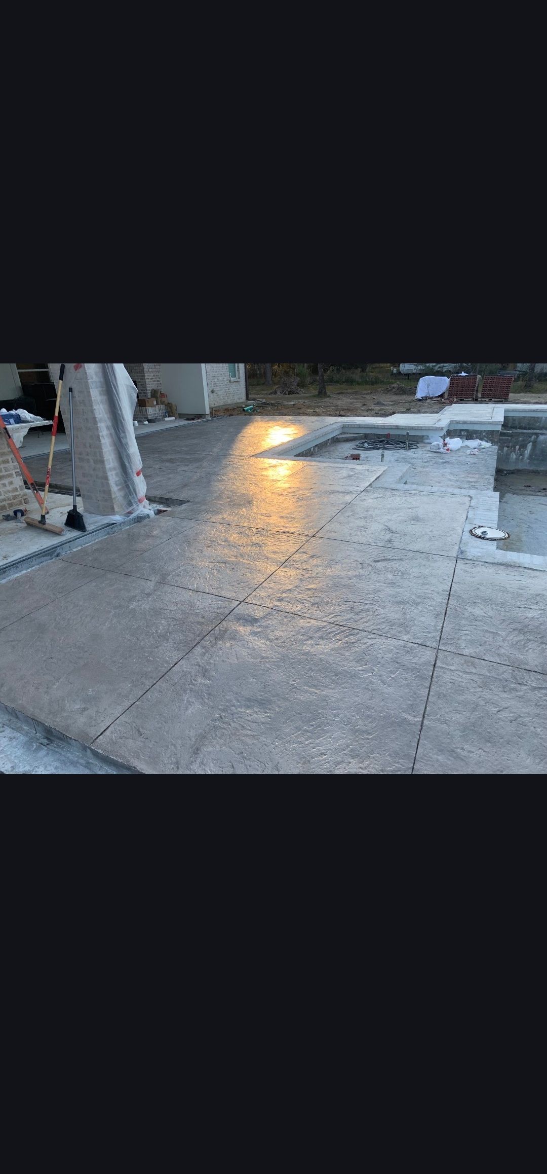 Worker leveling wet concrete on a construction site with wooden forms and rebar.
